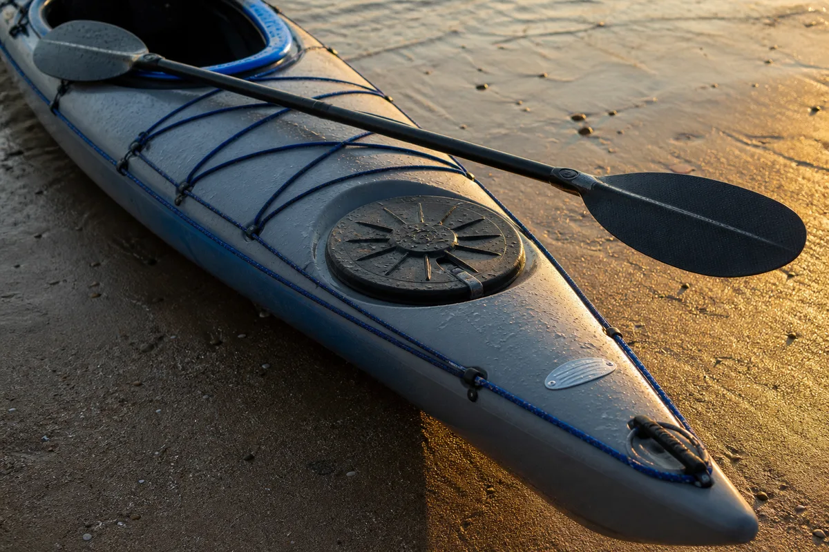 Kayak de mer rigide posé sur le sable, plaque signalétique et caissons étanches visibles